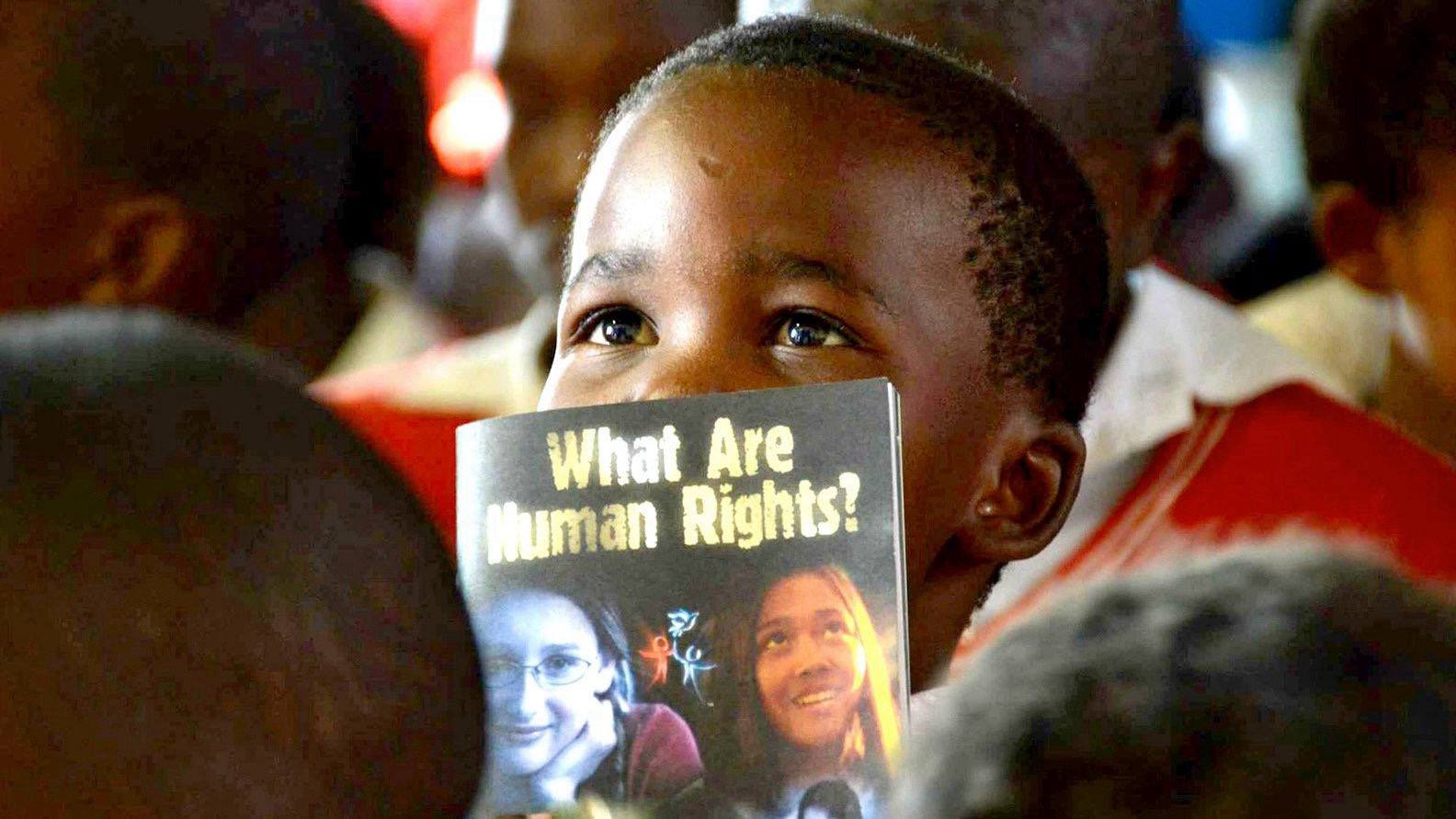 A young child holding a 'What Are Human Rights?' booklet